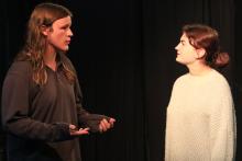 Two actors face each other on stage while rehearsing a scene.