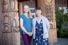 VIU Psychedelic-assisted Therapy Program Chair Shannon Dames with VIU Elder-in-Residence C-tasi:a Geraldine Manson standing outside in front of totem poles and smiling at the camera