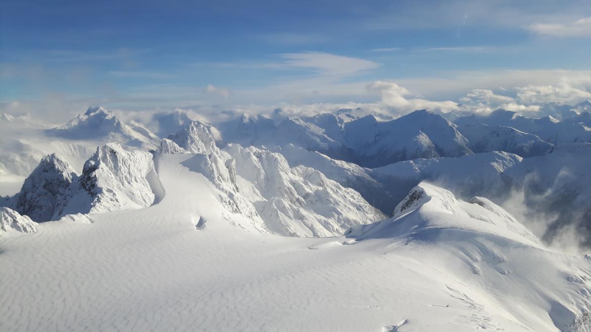 Mountain peaks covered in snow with a cloudy blue sky overhead.