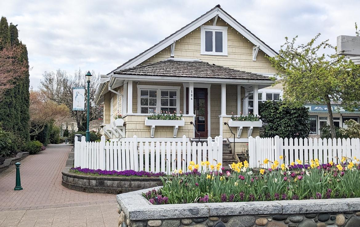 A building painted yellow with a white picket fence around it and a flower box with tulips out front.