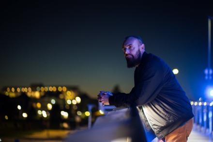 Shanon Sinn leans on a balcony railing and gazes at a night city scape