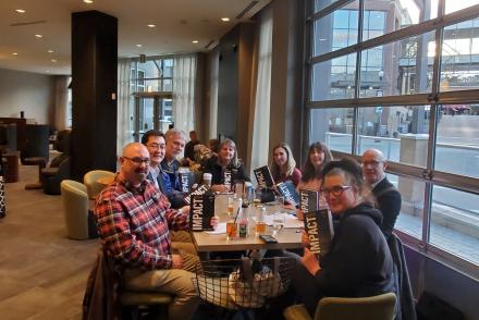 A group of people sit at a table, all holding copies of the same book